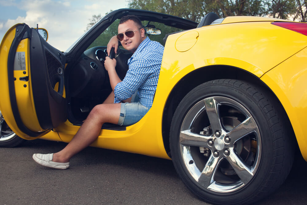 A young man sits in a sporty yellow convertible - cheap car insurance.