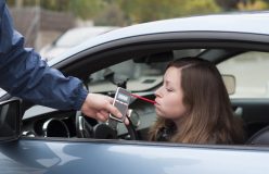 Young woman blowing into a breathalyzer after getting pulled over by a police officer - cheap SR22 insurance.