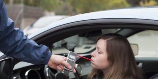 Young woman blowing into a breathalyzer after getting pulled over by a police officer - cheap SR22 insurance.