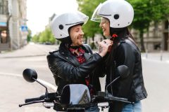 A couple gets ready for a motorcycle ride, the man adjusts the woman's helmet - cheap motorcycle insurance.