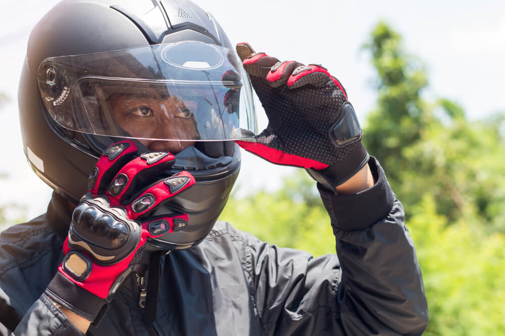 An African American man adjusts the visor on his motorcycle helmet - cheap motorcycle insurance.