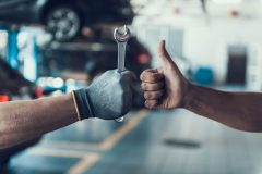 Mechanic giving a thumbs-up while holding a wrench next to a driver who brought his car for repair to his nearby local repair shop - Acceptance, cheap auto insurance