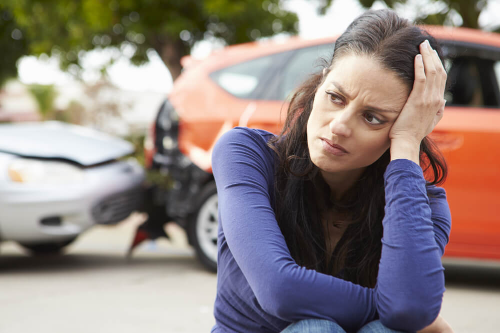 Concerned woman sitting on the street after a car crash
