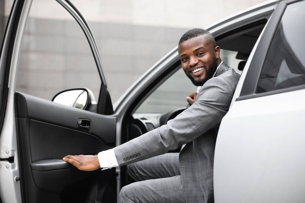 Cheerful black man in a nice suit getting out from behind the wheel of his car.