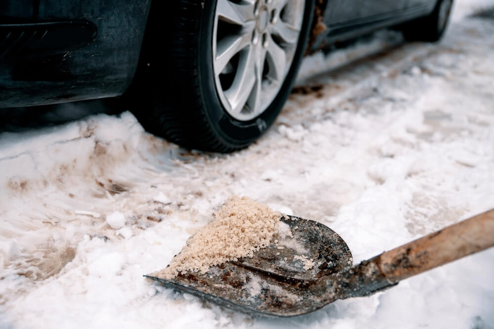 Shovel with salt on snowy driveway