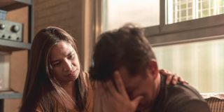 Man upset with head in his hands while his wife comforts him.