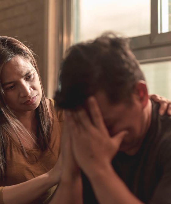 Man upset with head in his hands while his wife comforts him.