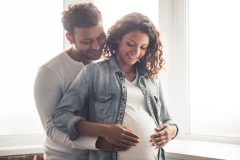 Young couple man behind embracing his pregnant wife with both their hands on her stomach - cheap car insurance.