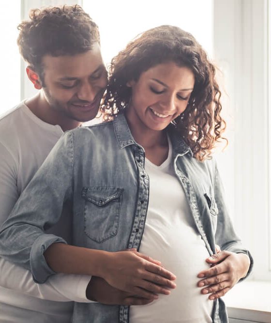 Young couple man behind embracing his pregnant wife with both their hands on her stomach - cheap car insurance.