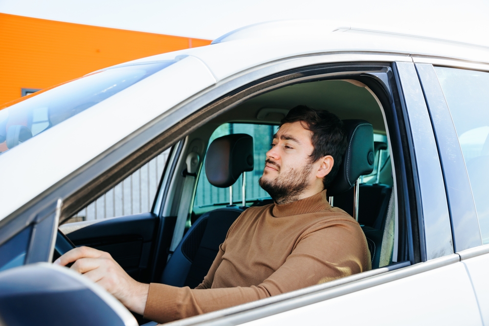 Young man sits behind the wheel of his car - cheap car insurance in California.