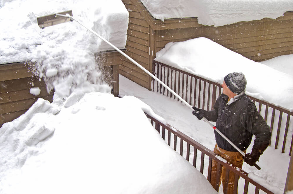 Man uses a snow rake to remove snow from the roof - cheap homeowners insurance.