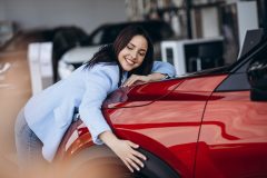 Happy woman smiling hugging new red car.