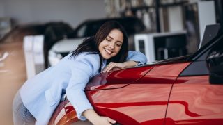 Happy woman smiling hugging new red car.