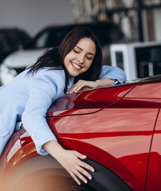 Happy woman smiling hugging new red car.