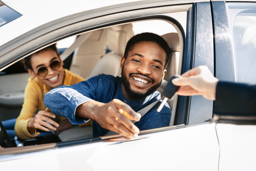 Happy black couple receiving car keys after buying new car while sitting in their car.