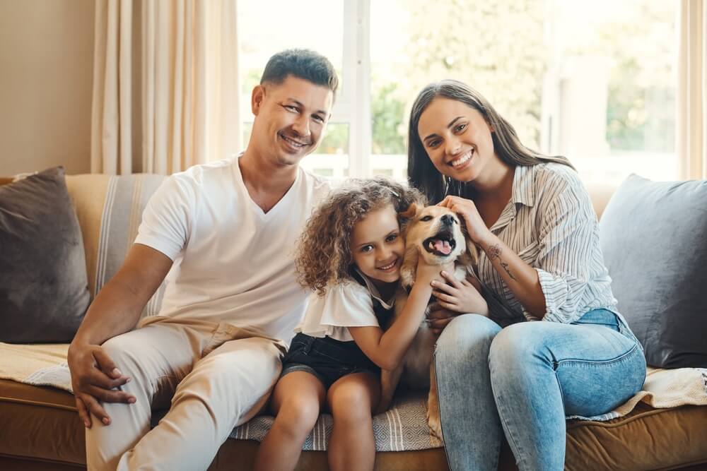 Mother, father and child sit on couch at home with their dog.