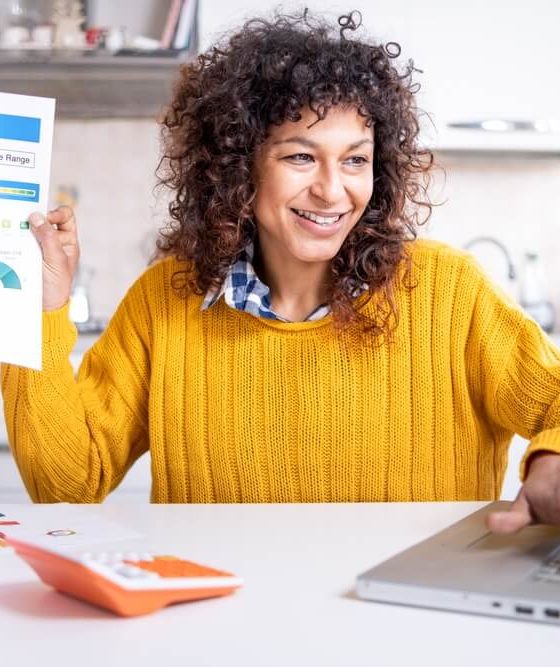 Woman buying car insurance on laptop holds her credit report in her other hand - cheap car insurance regardless of credit score.