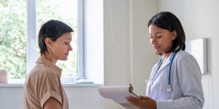 A young woman sits on an exam table while her doctor talks to her - cheap health insurance in California.