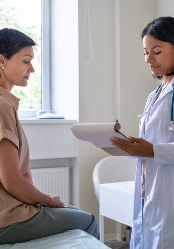 A young woman sits on an exam table while her doctor talks to her - cheap health insurance in California.