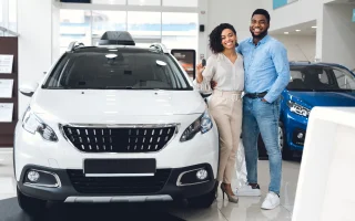 New Family Car. Cheerful Husband And Wife Holding New Automobile Key Smiling To Camera Standing Near Auto In Dealership Shop – Cheap car insurance.