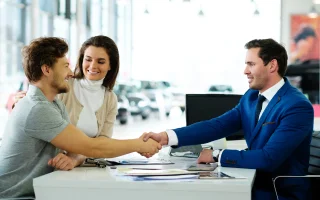 Salesman and customer shaking hands congratulating each other at the dealership showroom – cheap car insurance.