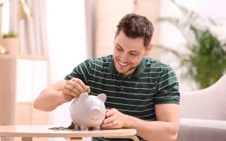 Man with piggy bank and money at home, concept of saving money with car insurance discounts – cheap car insurance.