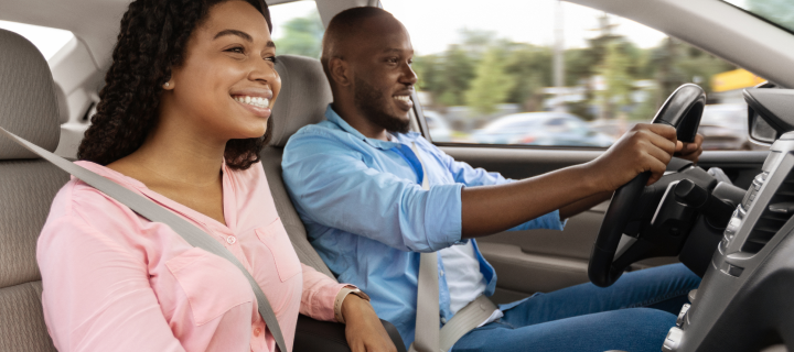 Happy African American man and woman going on summer vacation by car. Beautiful millennial couple sitting inside their new auto, young family cheerfully smiling looking at road, profile side view