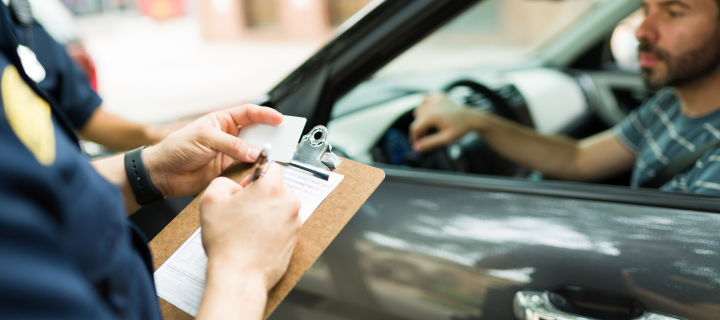 Close up of a police cop writing a traffic ticket or fine to a male driver in his car for speeding